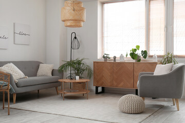 Interior of light living room with grey sofa, wooden cabinet and armchair