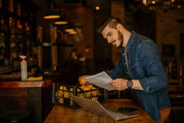 Male cafe owner checking inventory goods while calculating business expenses.