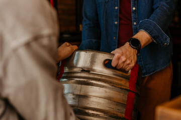 Worker carrying barrel with beer at the brewery and talking to the brewery owner. Focus on hands