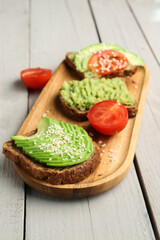 Board of tasty avocado toast on light wooden background