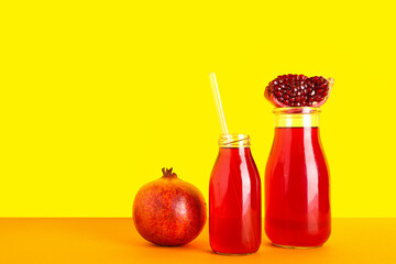 Bottles of fresh pomegranate juice on yellow background