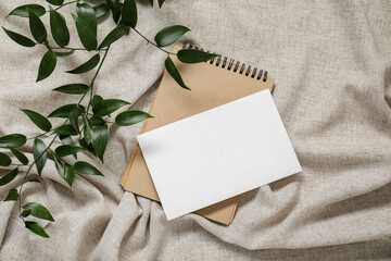 Blank invitation card, notebook and eucalyptus branches on grey crumpled tablecloth