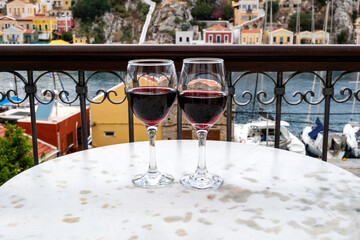 Two Glass of Red Wines on a Marble Bistro and a View of the Main Port of Symi Island, Greece