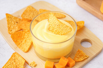 Board with bowl of tasty cheddar cheese sauce and nachos on white grunge background