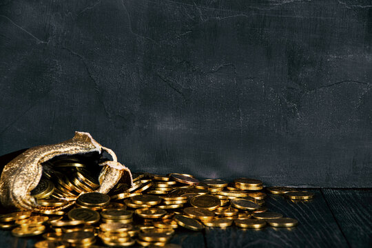 A bag with gold coins on a wooden background. The money is in a black bag. Treasure Hunt. A Purse with money on a black background. Wallet wit gold coins.Copy space