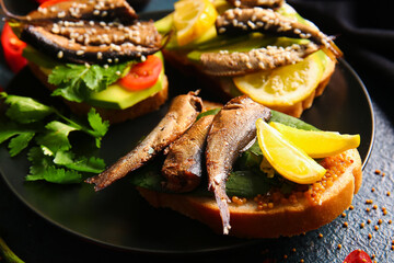 Plate of tasty sandwiches with canned smoked sprats on black background