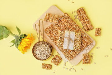 Measuring cups with tasty kozinaki and seeds on pale yellow background