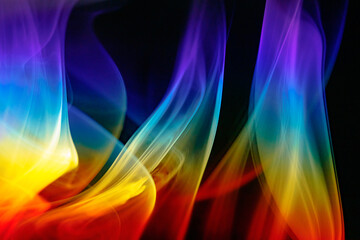 Colorful fire like wavy rainbow incense smoke under prism light flowing upward inside dark studio