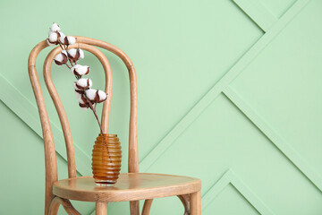 Cotton sprig in vase on wooden chair near green wall