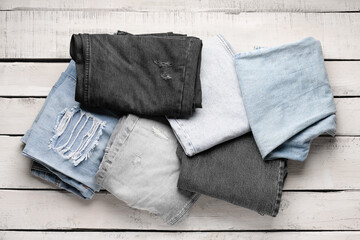 Different stylish denim jeans on wooden background