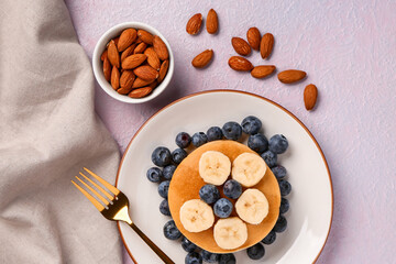 Plate with sweet pancakes, banana, blueberry and nuts on pink background