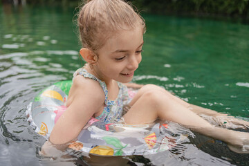 Child with inflatable toy ring float in swimming pool. Little girl learning to swim and dive in outdoor pool of tropical resort. Swimming with kids. Healthy sport for children. Water fun