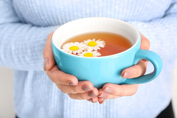 Beautiful young woman with cup of chamomile tea near white wall