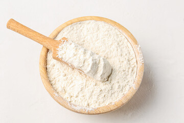Fototapeta na wymiar Wooden bowl with wheat flour and scoop on white background