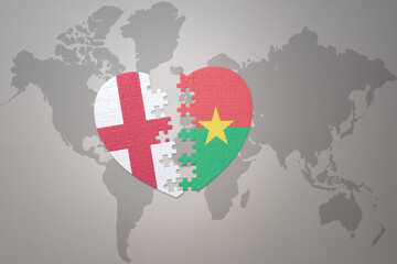 puzzle heart with the national flag of burkina faso and england on a world map background.Concept.