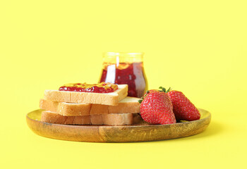 Wooden plate with toasts, jar of tasty jam and fresh strawberry on yellow background
