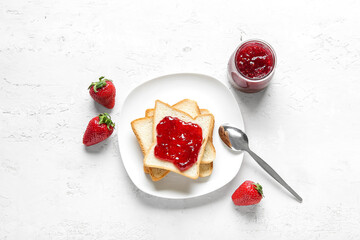 Plate with toasts, jar of tasty strawberry jam and spoon on grunge white background
