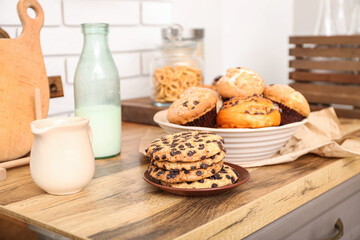 Bottle with milk, cookies and cupcakes on wooden table in kitchen