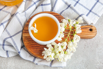 Bowl of honey with flowers of acacia on light background, closeup