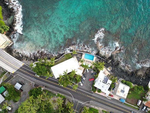 View of coastal Kailua-Kona on the Big Island of Hawai'i. Aerial drone looking down from directly overhead along the coast with palm trees, houses, condominiums, and blue ocean water.