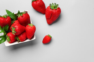 Bowl with fresh strawberries and mint on grey background