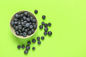 Bowl with fresh blueberries on green background