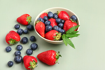 Bowl with fresh blueberries and strawberries on green background
