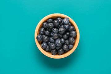Bowl with fresh blueberries on blue background