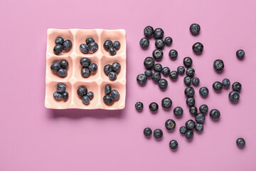 Ice cube tray with fresh blueberries on lilac background