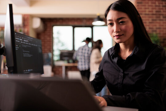 Asian freelance coder analyzing compiling html code on computer display, working on interface development. Programming engineer using terminal window with firewall server data in it big data agency