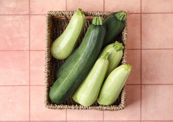 Wicker basket with raw zucchini on beige tile background