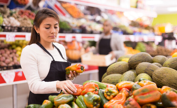 Supermarket woman worker in black apron putting vegetables in her department