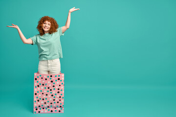 Happy overjoyed funny ginger hipster girl in casual clothes jumping out appeared from huge paper...