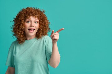 Surprised excited attractive young ginger woman wearing casual clothes and smiling pointing finger...