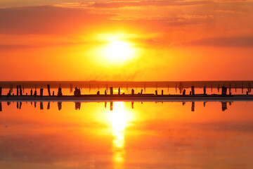 Fototapeta na wymiar Orange sunset, dramatic and majestic sky over beach with sun reflection in water. Wood posts for salt extraction of extremely salty lake, Ukraine. Summer season, idyllic peaceful dusk sunlight