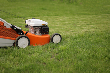 Close up orange-grey electric lawn mower on bright lush green lawn. Gardening work tools. Rotary lawn mower machine cut grass. Professional lawn care service. Place for text