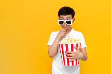 pensive asian little boy of ten years old wearing 3d glasses and with popcorn thinks and imagines