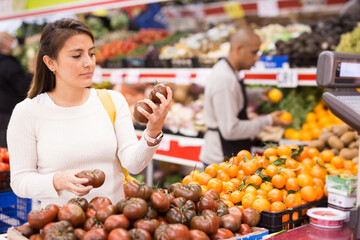 Satisfied female customer choosing fresh black tomatoes in food shop