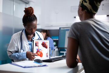 Doctor explaining heart informations to patient on tablet at clinic desk. Cardiologist providing...