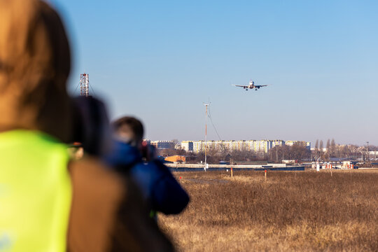 Group of many people watching planes landing and take off airport runway field planespotting conference warm morning time. Planespotters in safety vest waiting aicraft arrival approaching departure