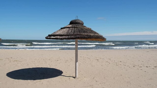 Straw beach rattan parasol at the empty beach with blue sky backgrounds sea ocean coast. Relaxing day. Idyllic travel and summer vacation concept. Straw umbrella on beautiful tropical beach. 