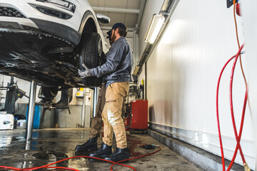 Car mechanics installing a new car wheel on a vehicle on a hoist in auto repair shop. High quality...