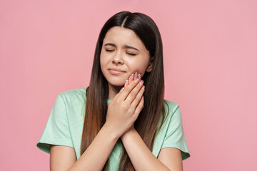 Portrait of sad teenage girl touching cheek, toothache isolated on pink background, dental care