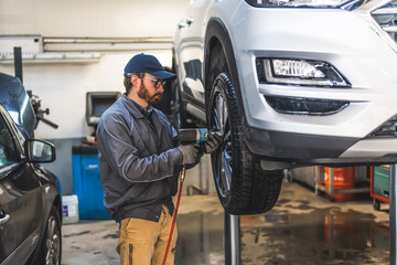 Car mechanic using pneumatic wrench to replace wheel of a vehicle on a hoist . High quality photo