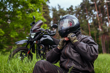Fototapeta premium Close up of biker unfastening helmet after riding motobike in summer forest. Man wearing leather clothes outdoors.