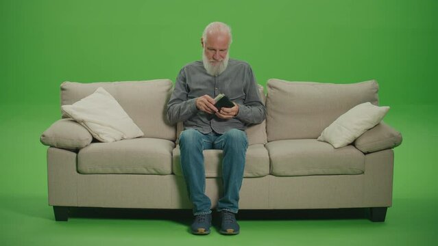 Green Screen. A Poor Old Man with Gray Beard Counting His Money in US Dollars. An Elderly Man is Stressed by the Amount of US Dollar Money in His Wallet. Survival in Retirement.