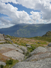 panoramic view of plateau on rocky mountain top - with background of mountains overhung by clouds and blue sky