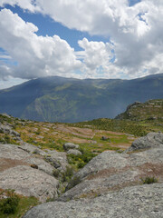 panoramic view of plateau on rocky mountain top - with background of mountains overhung by clouds and blue sky