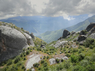 view on a mountainside with bushes and rocks overlooking the valley with a background of mountains...