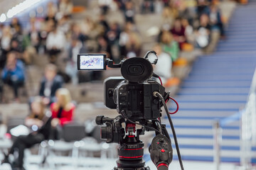 Video recording of conferences and events in the auditorium. A video camera on a tripod is filming the audience, close-up. Spectators in the hall out of focus